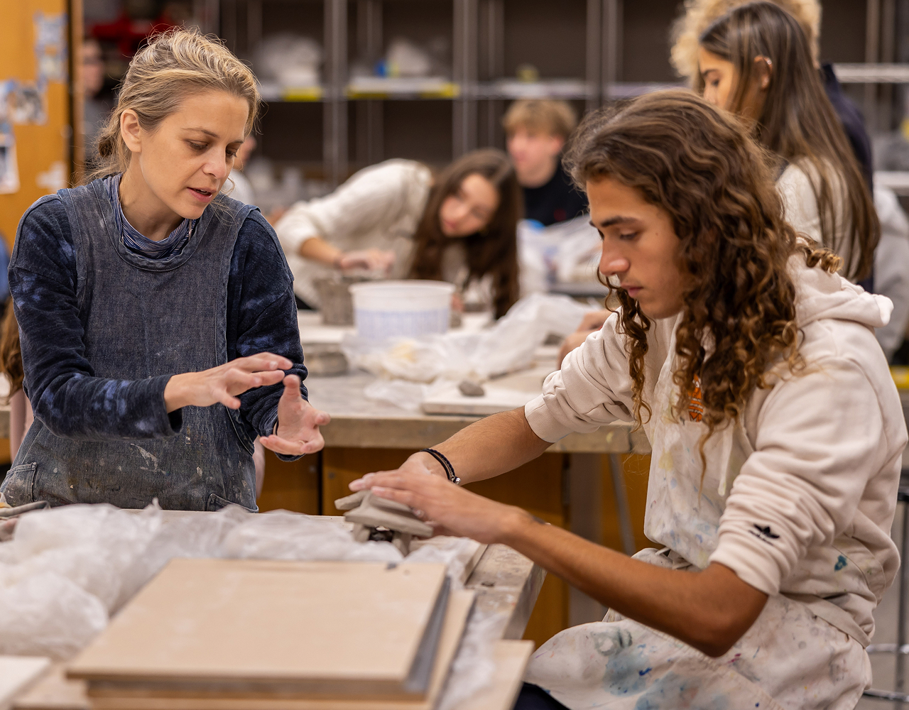 A young male high school student works with clay in Arts class