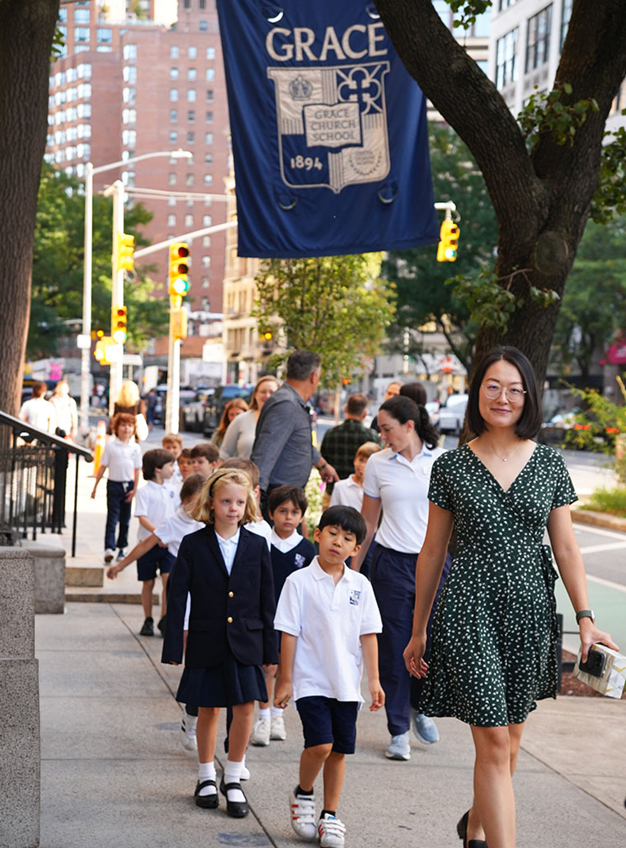 a Lower School teacher walking students outside under a Grace Church School flag.